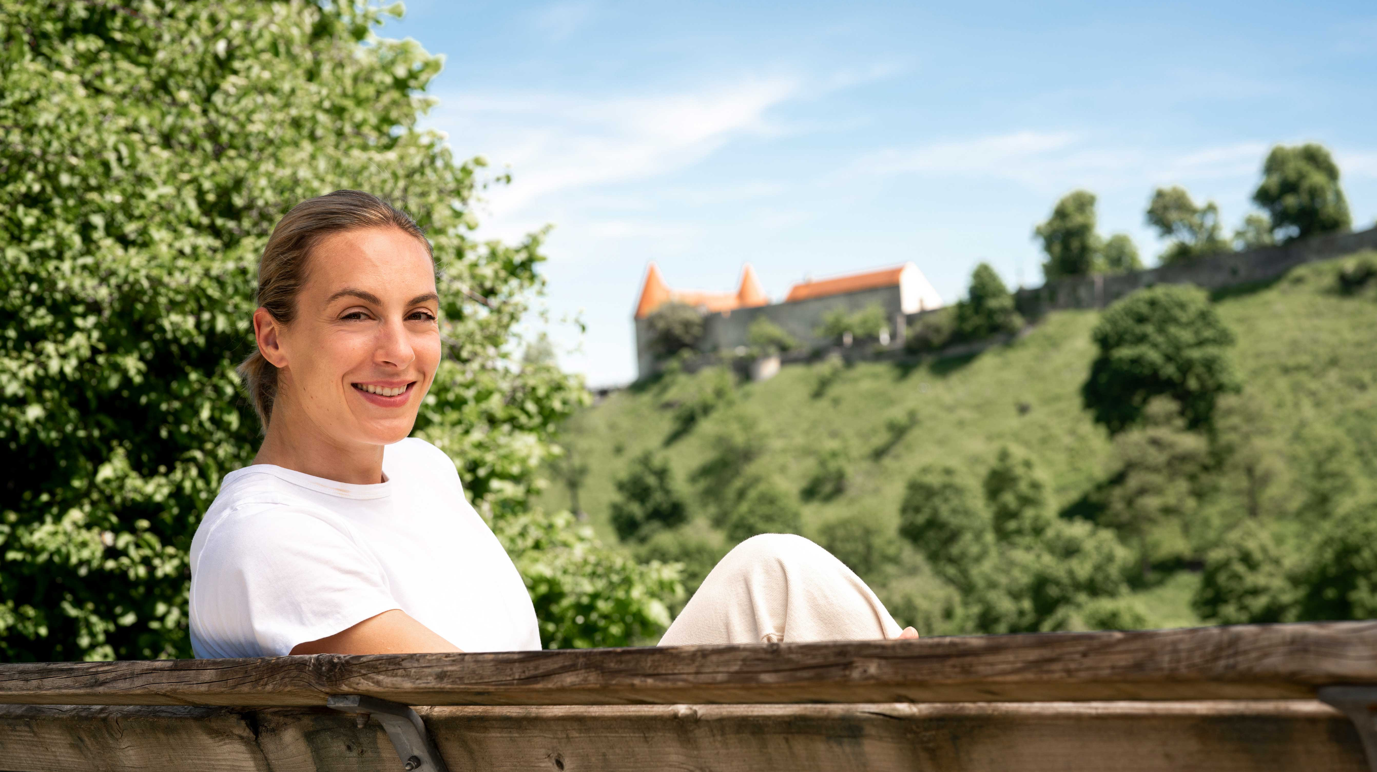 Eine Frau sitzt unterhalb der Burg zu Burghausen und lächelt in die Kamera